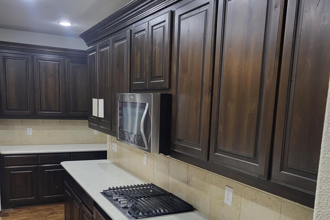 Kitchen with refinished dark stained cabinets running to the ceiling above a light quartz countertop