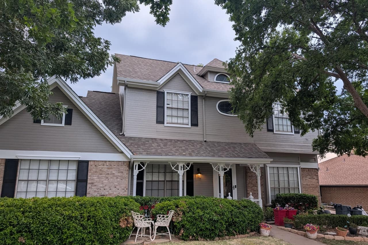 Two-story home with freshly painted taupe siding, white trim and black shutters, shaded by a large tree