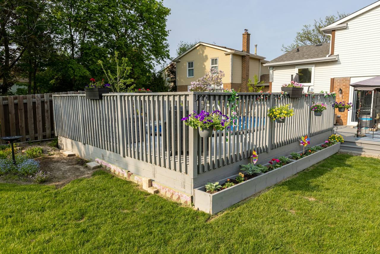 Backyard wood fence painted soft gray, lined with flower boxes in a suburban yard